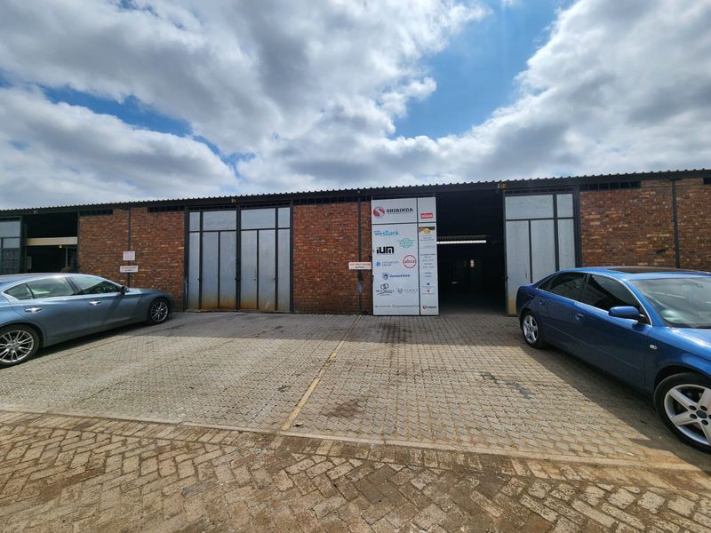 Front exterior view of an industrial warehouse facility featuring brick construction, large sliding access doors, and a paved parking area with tenant signage.