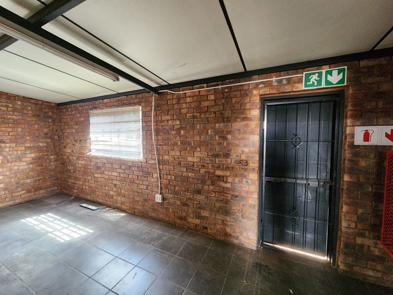 An empty industrial-style office space featuring exposed brick walls, tiled flooring, a security gate, and essential fire safety signage.