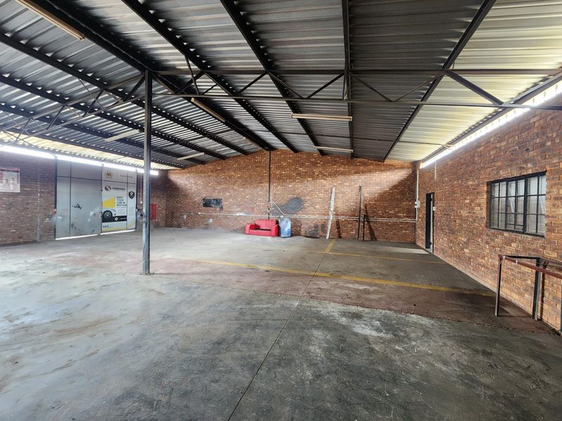Spacious industrial utility area featuring exposed brick walls, concrete flooring, and a high-clearance corrugated metal roof, suitable for workshop or storage use.