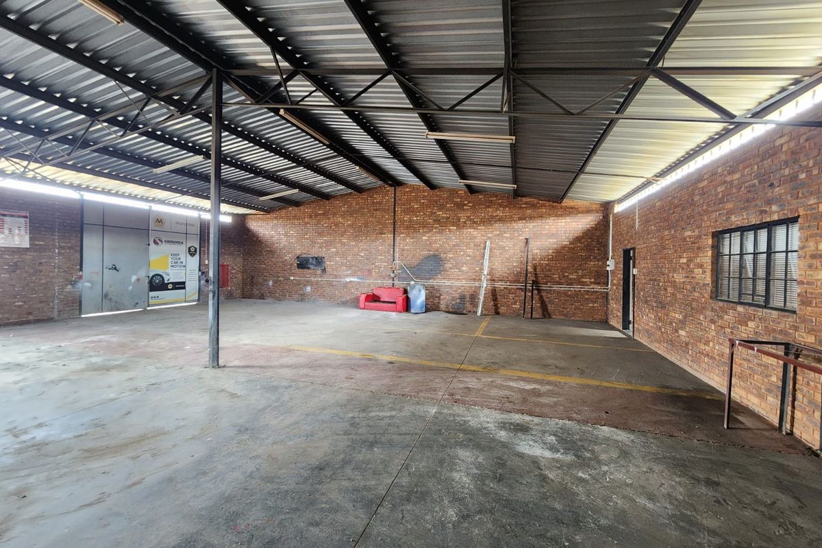 Spacious industrial utility area featuring exposed brick walls, concrete flooring, and a high-clearance corrugated metal roof, suitable for workshop or storage use.