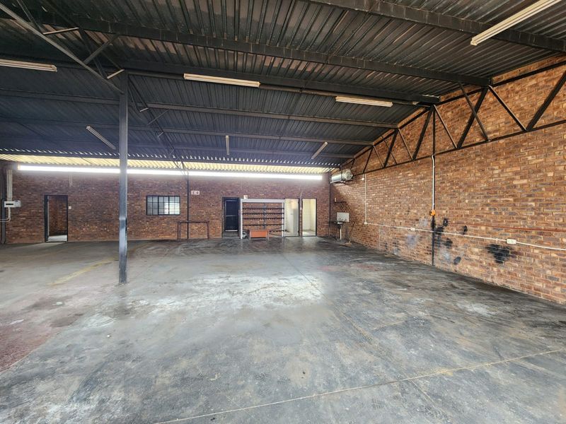 Spacious industrial utility area featuring exposed brick walls, concrete flooring, and a high corrugated metal roof, suitable for workshop or storage use.