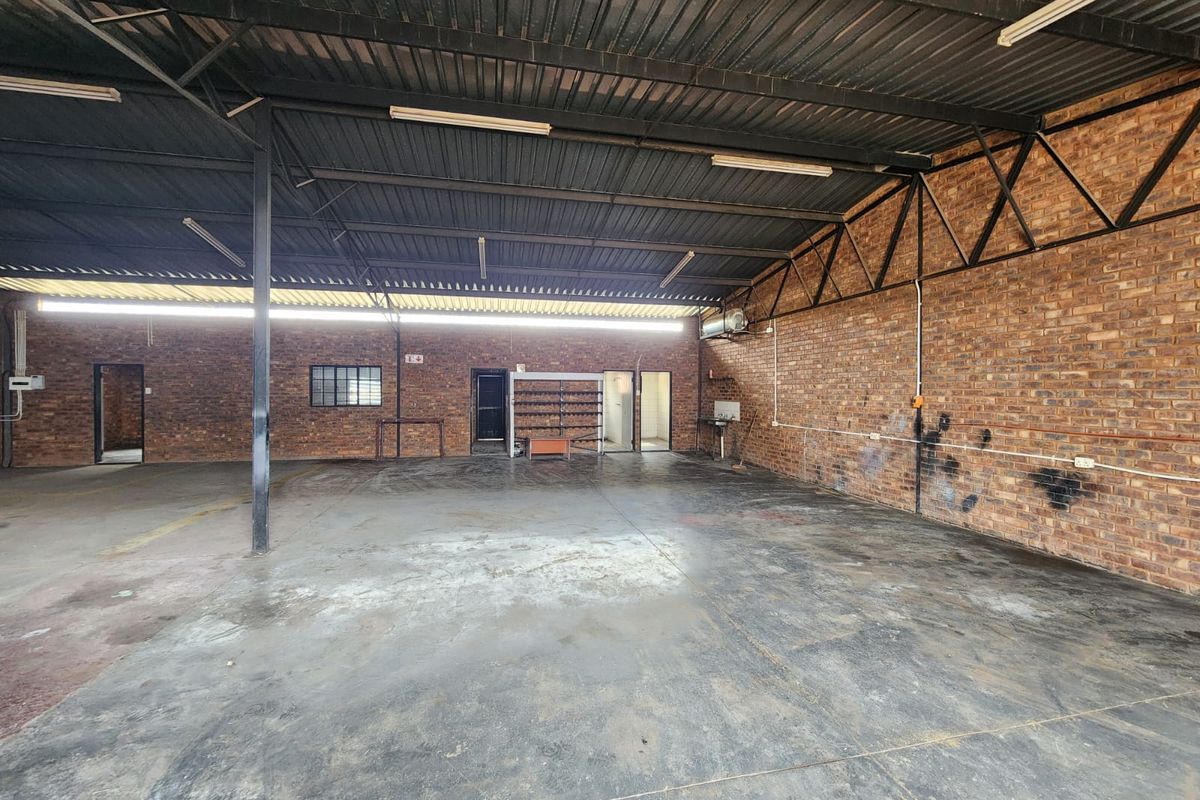Spacious industrial utility area featuring exposed brick walls, concrete flooring, and a high corrugated metal roof, suitable for workshop or storage use.