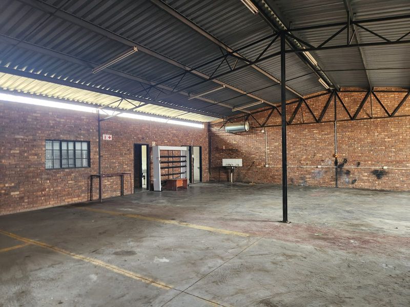 Spacious industrial utility area featuring exposed brick walls, concrete flooring, and high-clearance steel truss roofing, suitable for workshop or storage use.
