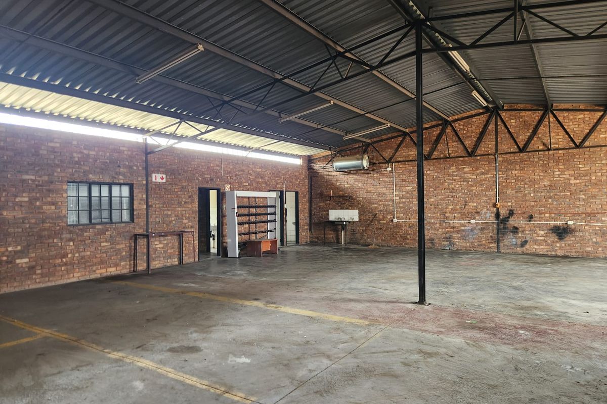 Spacious industrial utility area featuring exposed brick walls, concrete flooring, and high-clearance steel truss roofing, suitable for workshop or storage use.