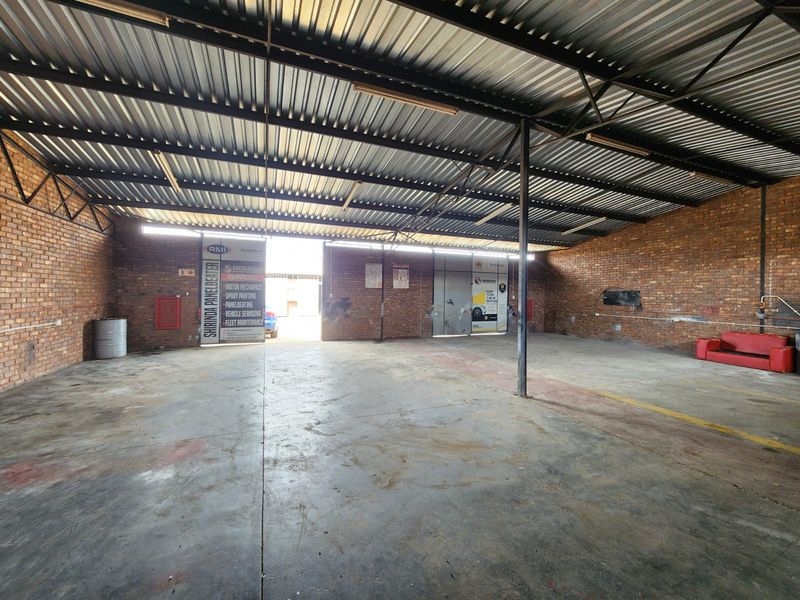 Spacious industrial garage featuring exposed brick walls, high corrugated metal roofing, and durable concrete flooring, suitable for workshop or storage use.