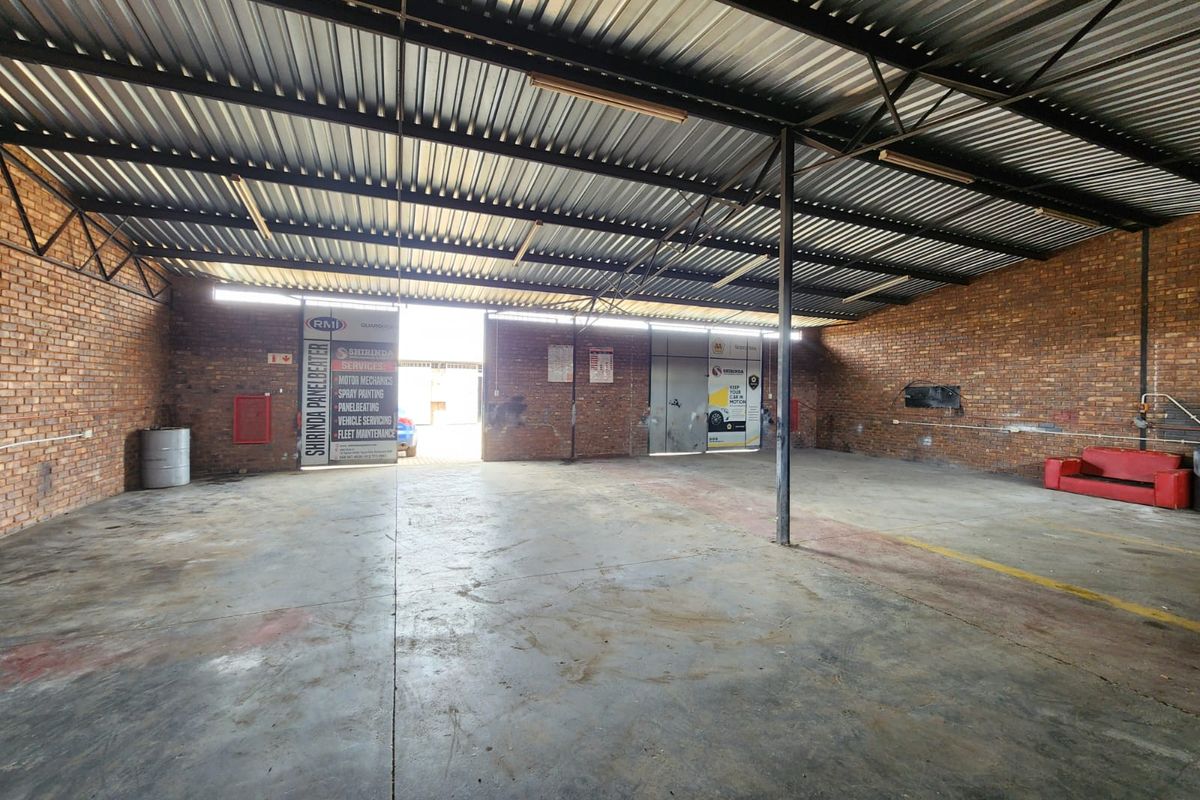 Spacious industrial garage featuring exposed brick walls, high corrugated metal roofing, and durable concrete flooring, suitable for workshop or storage use.