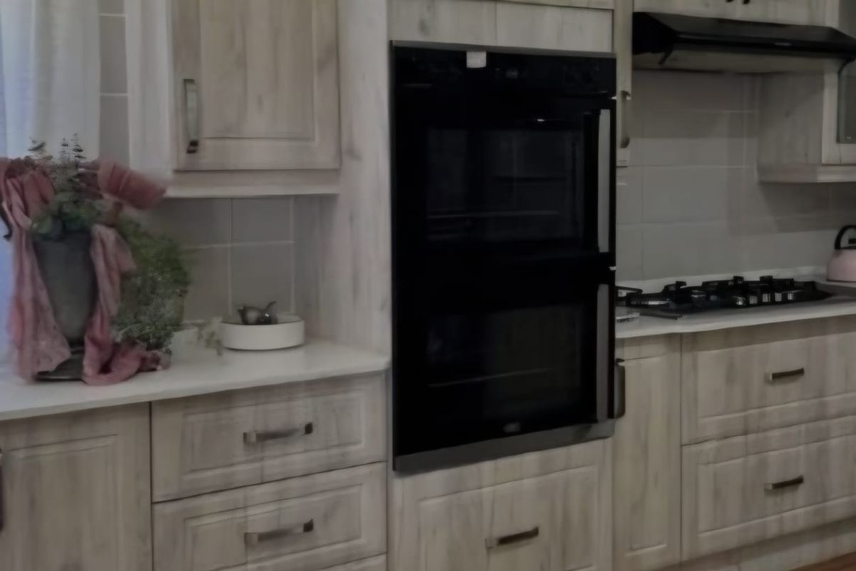A functional kitchen featuring light-toned wooden cabinetry, a built-in double oven, gas hob, extractor fan, and tiled flooring.