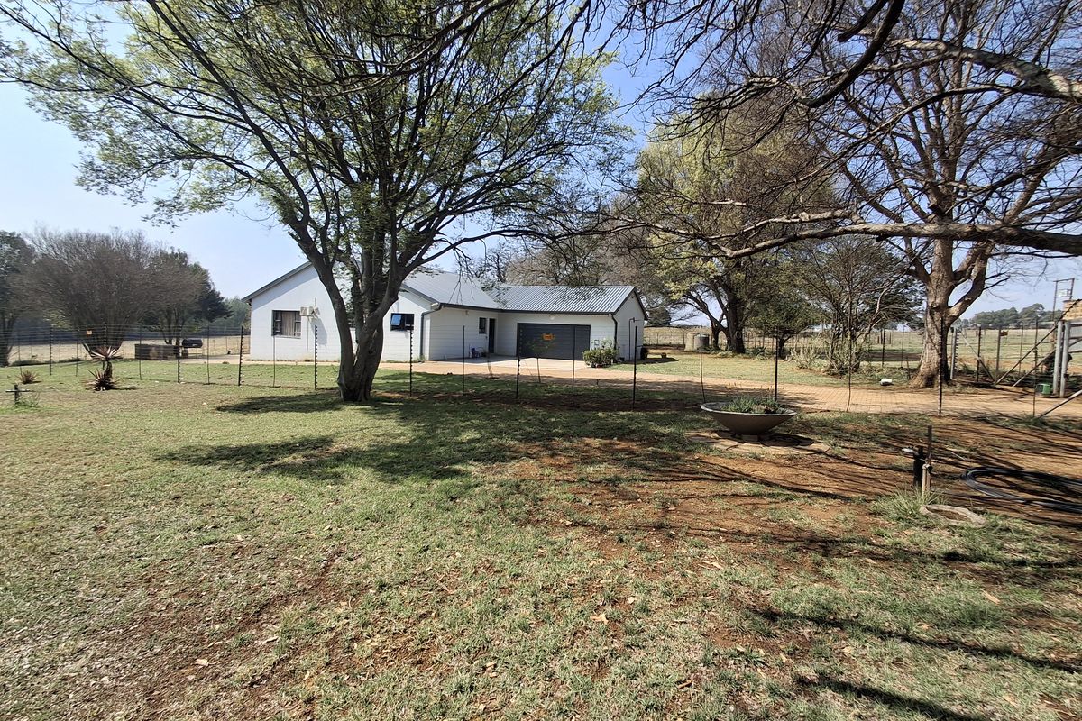 A view of the rear exterior of the farm property, featuring a metal roof, garage access, and surrounding garden space with mature trees.