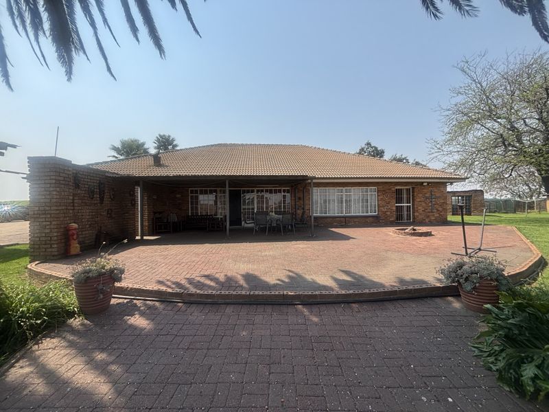 Rear view of the property featuring a spacious paved courtyard, a covered patio area, and a built-in fire pit, ideal for outdoor entertaining.