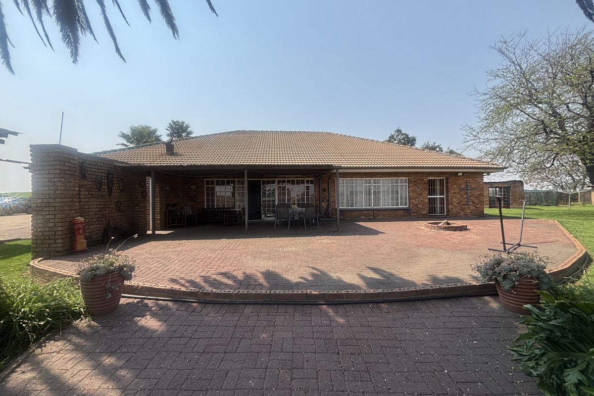 Rear view of the property featuring a spacious paved courtyard, a covered patio area, and a built-in fire pit, ideal for outdoor entertaining.