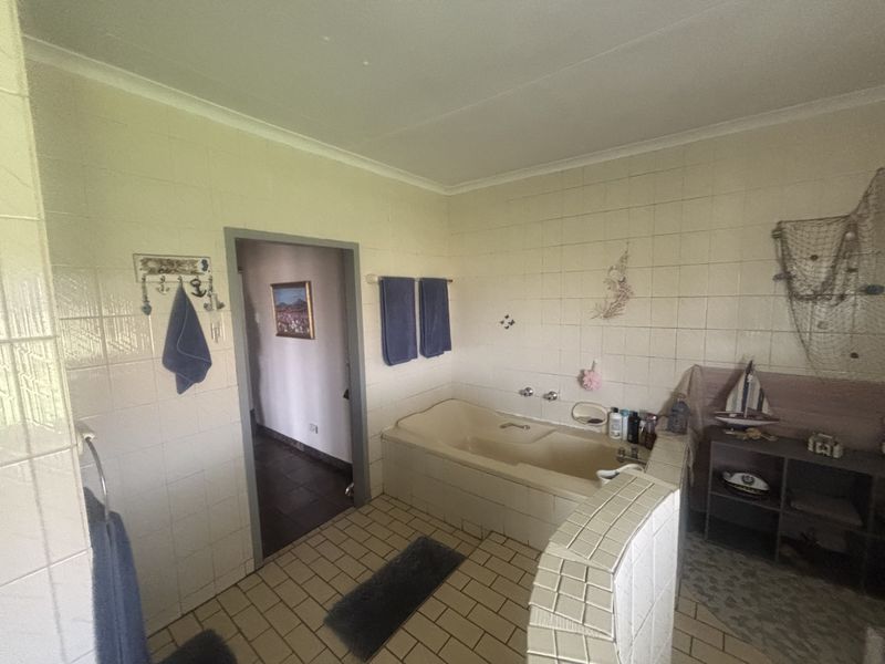 A dated bathroom featuring a built-in bathtub, tiled walls, and tiled flooring, offering a functional space with potential for modernization.
