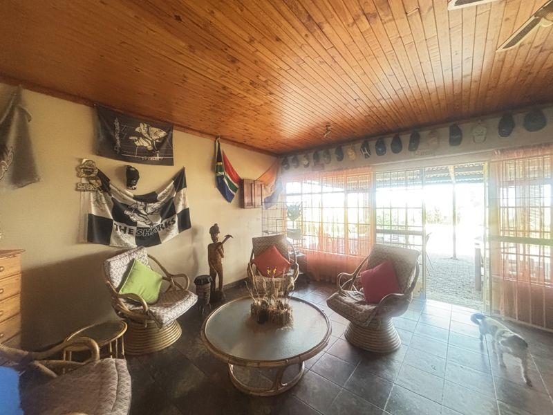 A living room featuring a warm wooden tongue and groove ceiling, tiled flooring, and a sliding glass door providing access to the outdoor area.