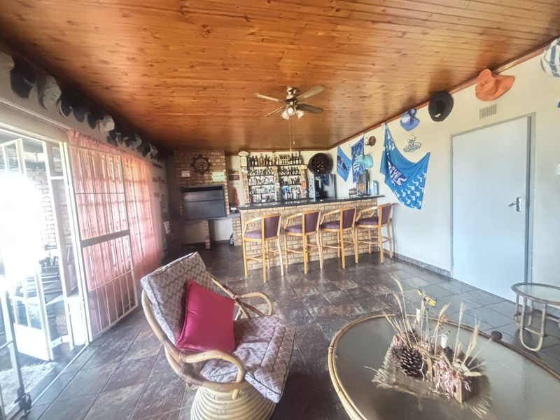 Spacious entertainment area featuring a built-in bar, indoor braai, timber ceiling, and tiled flooring, offering a functional space for social gatherings.