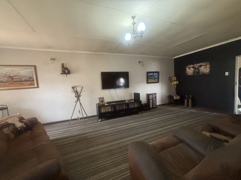 A spacious living room featuring neutral walls with a dark accent wall, carpeted flooring, and overhead lighting.