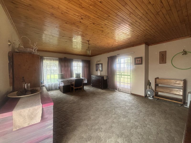 Spacious living area featuring a traditional knotty pine ceiling, carpeted flooring, and direct access to the exterior via a security gate.