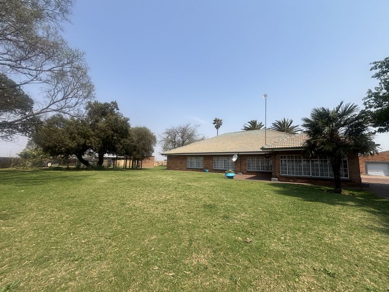 A spacious rear exterior view of a brick-built small holding featuring a large, well-maintained lawn and mature garden trees.