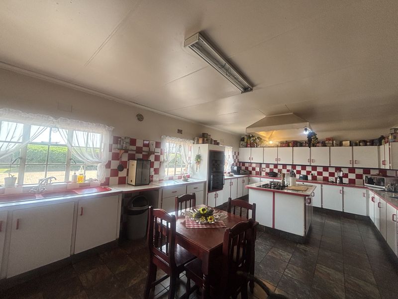 Spacious kitchen featuring extensive built-in cabinetry, a central island with a gas hob, tiled backsplash, and double sink, offering a functional layout.