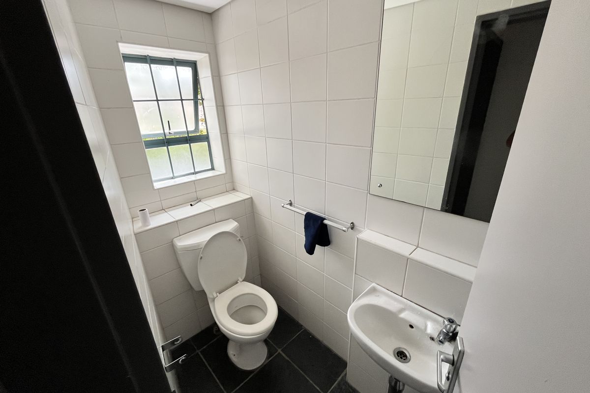 A compact office restroom featuring white wall tiles, dark floor tiles, a wall-mounted basin, and a standard toilet.