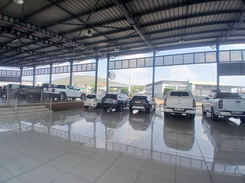 Spacious open-plan retail showroom featuring high steel-truss ceilings, polished tiled flooring, and a raised display platform with metal railings.