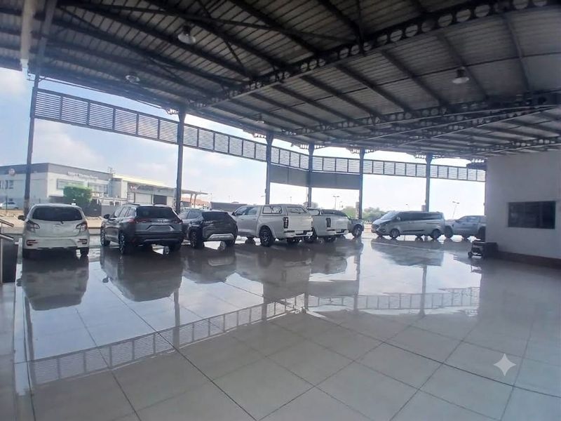 A large, open-plan commercial garage or showroom space featuring high steel roofing and polished tiled flooring, suitable for vehicle display or storage.