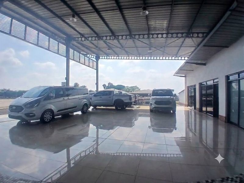 A spacious, covered retail or showroom area featuring high-quality tiled flooring, steel structural framing, and large glass entrance doors.