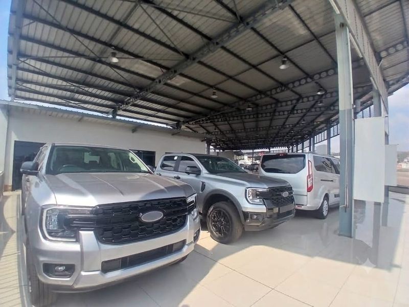 A spacious, covered retail garage or showroom area featuring high-clearance steel roofing, tiled flooring, and industrial lighting, suitable for vehicle display.