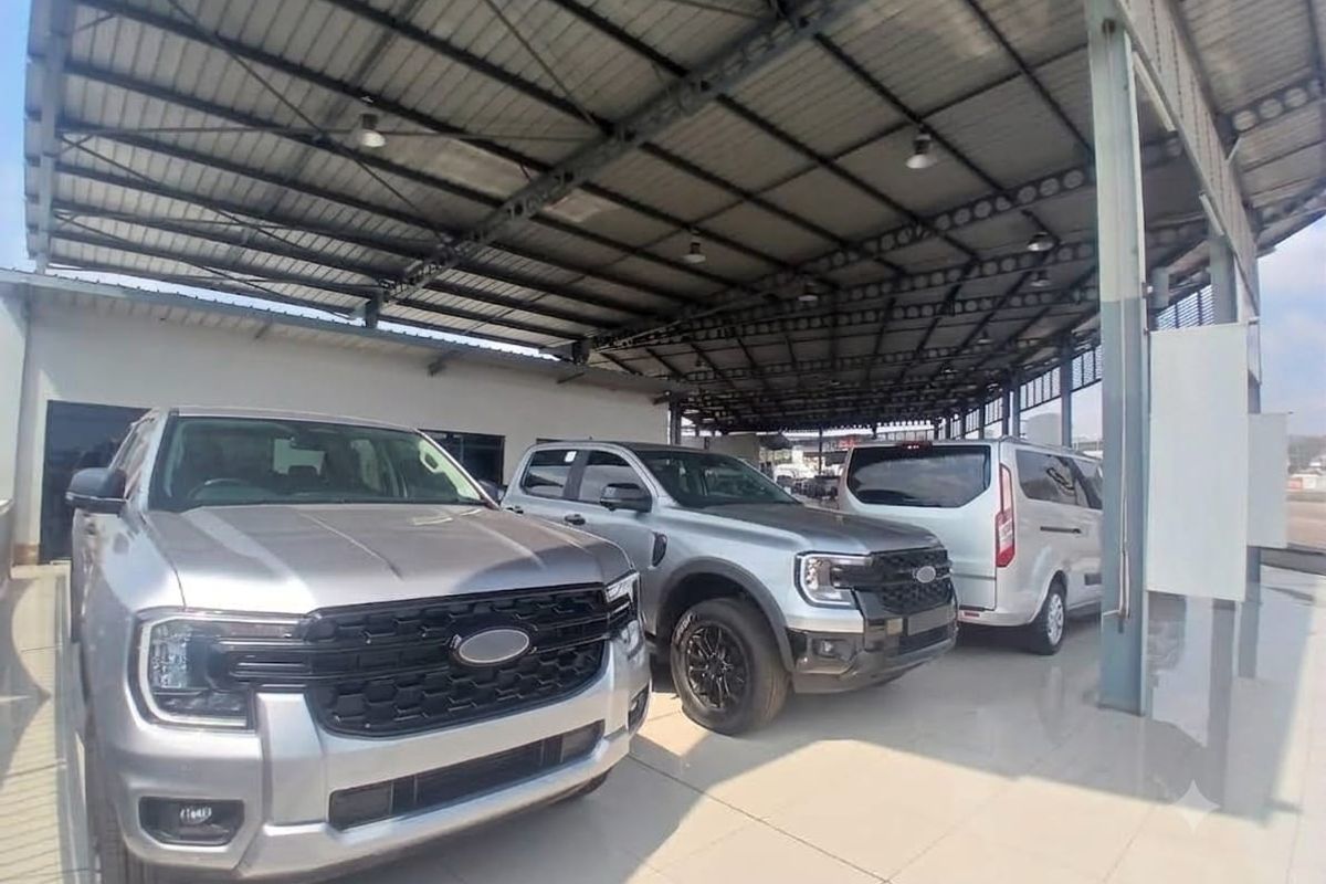 A spacious, covered retail garage or showroom area featuring high-clearance steel roofing, tiled flooring, and industrial lighting, suitable for vehicle display.