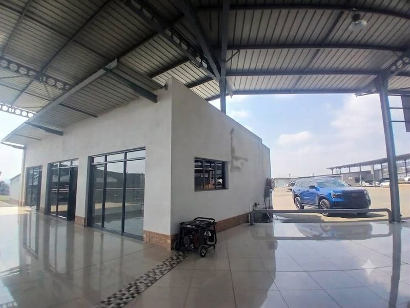 A covered outdoor retail or commercial space featuring tiled flooring, aluminium glass doors, and a large metal roof structure.