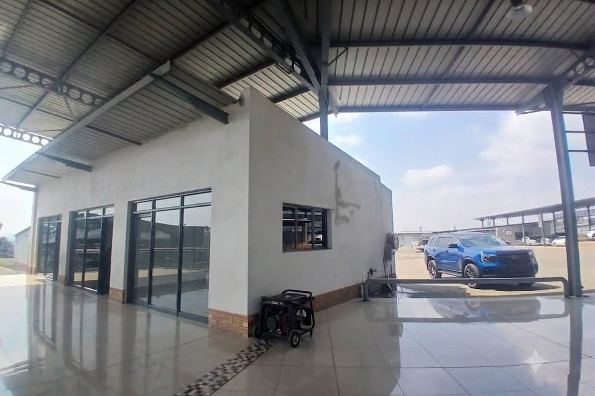 A covered outdoor retail or commercial space featuring tiled flooring, aluminium glass doors, and a large metal roof structure.