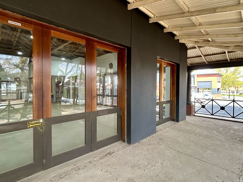 Front exterior view of a retail space featuring a covered veranda, concrete flooring, and large timber-framed glass sliding entrance doors.