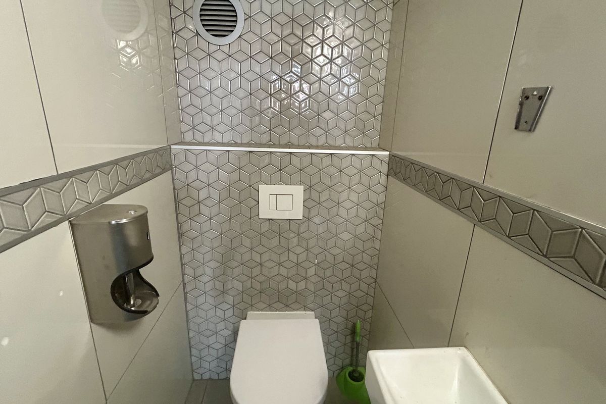 A compact, modern bathroom featuring tiled walls with geometric accents, a wall-mounted toilet with a flush plate, and a small wall-mounted basin.