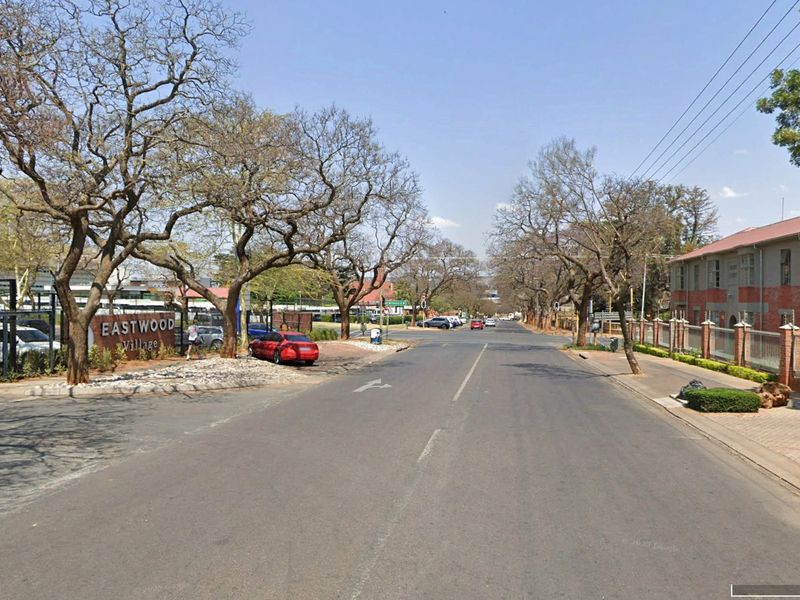 Street view of the neighborhood approach showing the Eastwood Village signage, mature trees, and surrounding commercial building infrastructure.