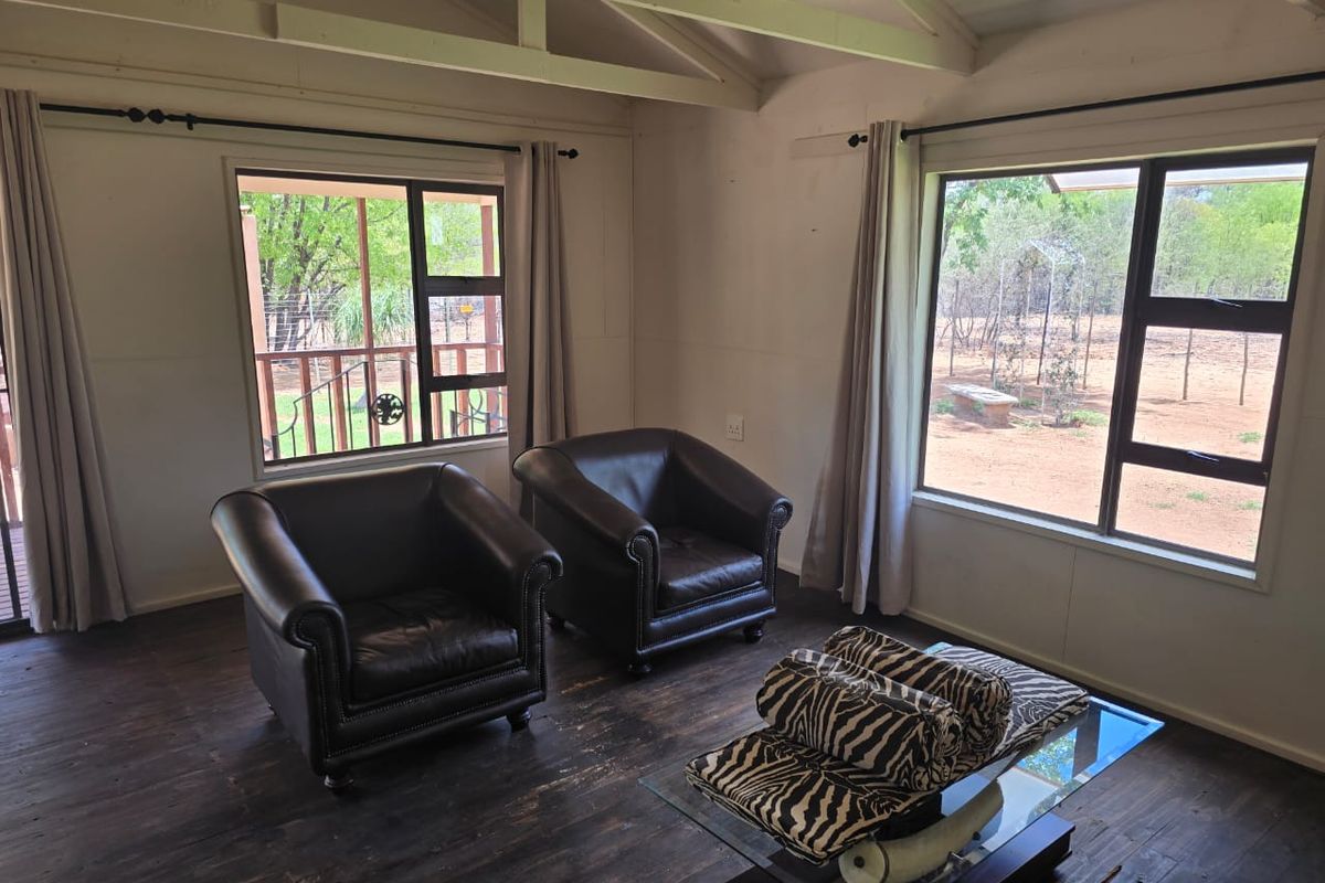 A bright living area featuring exposed timber ceiling beams, dark wood flooring, and large windows providing views of the surrounding farm landscape.