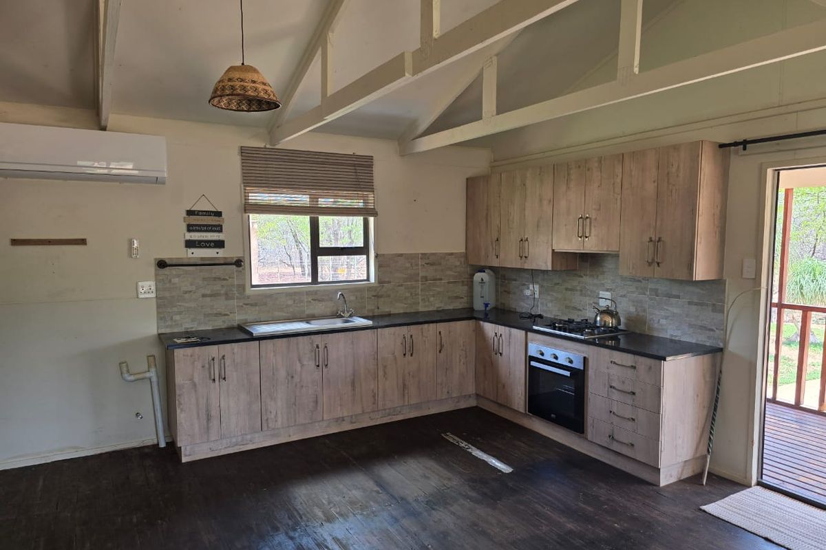 A functional kitchen featuring wood-look cabinetry, dark countertops, a built-in oven and hob, and vaulted ceilings with exposed beams.