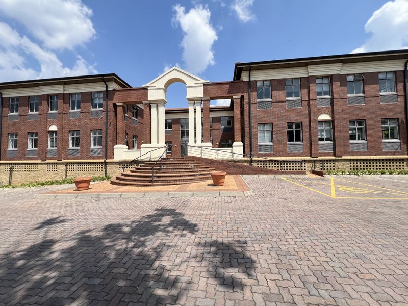 A professional exterior view of a multi-story brick office building featuring a prominent arched entrance, paved driveway, and well-maintained architectural detailing.