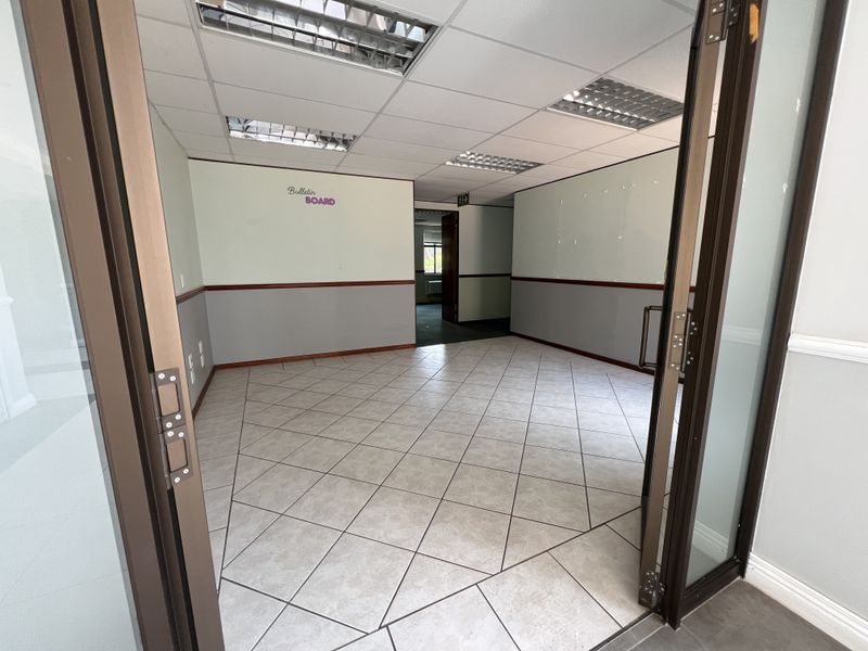 An empty office space featuring ceramic tile flooring, a suspended ceiling with recessed lighting, and glass panel double doors.