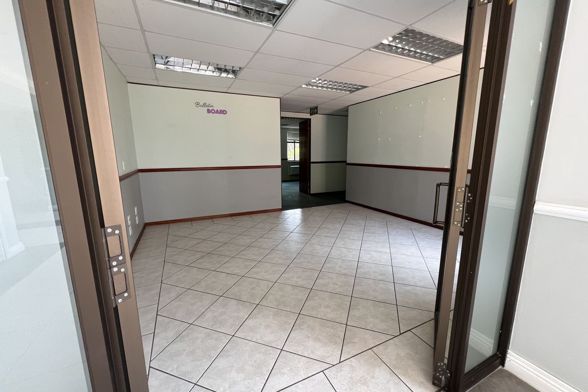 An empty office space featuring ceramic tile flooring, a suspended ceiling with recessed lighting, and glass panel double doors.