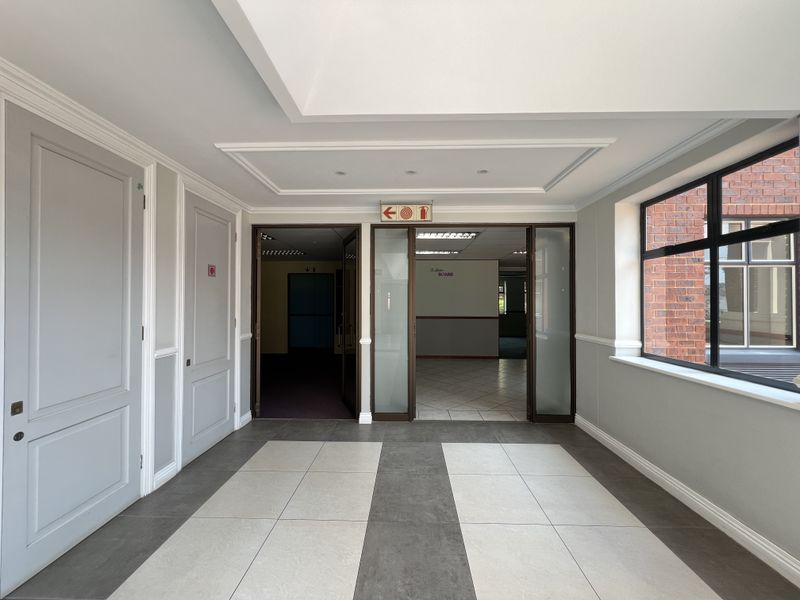A bright and spacious office entrance area featuring modern tiled flooring, recessed ceiling details, and glass-panelled doors leading into the main office space.