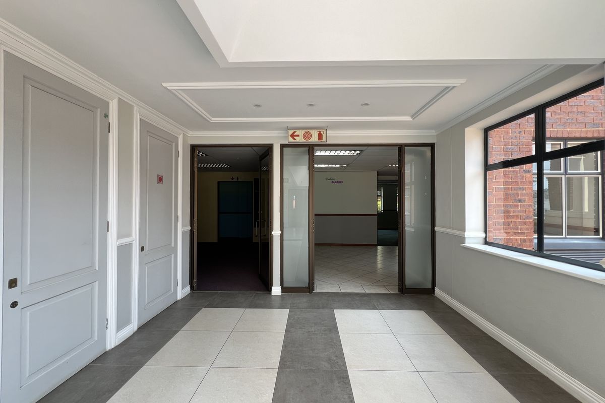 A bright and spacious office entrance area featuring modern tiled flooring, recessed ceiling details, and glass-panelled doors leading into the main office space.