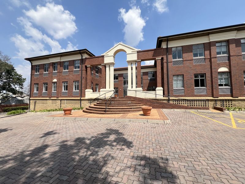 A professional office building featuring a classic red brick facade, a prominent arched entrance with stone steps, and a paved parking area.
