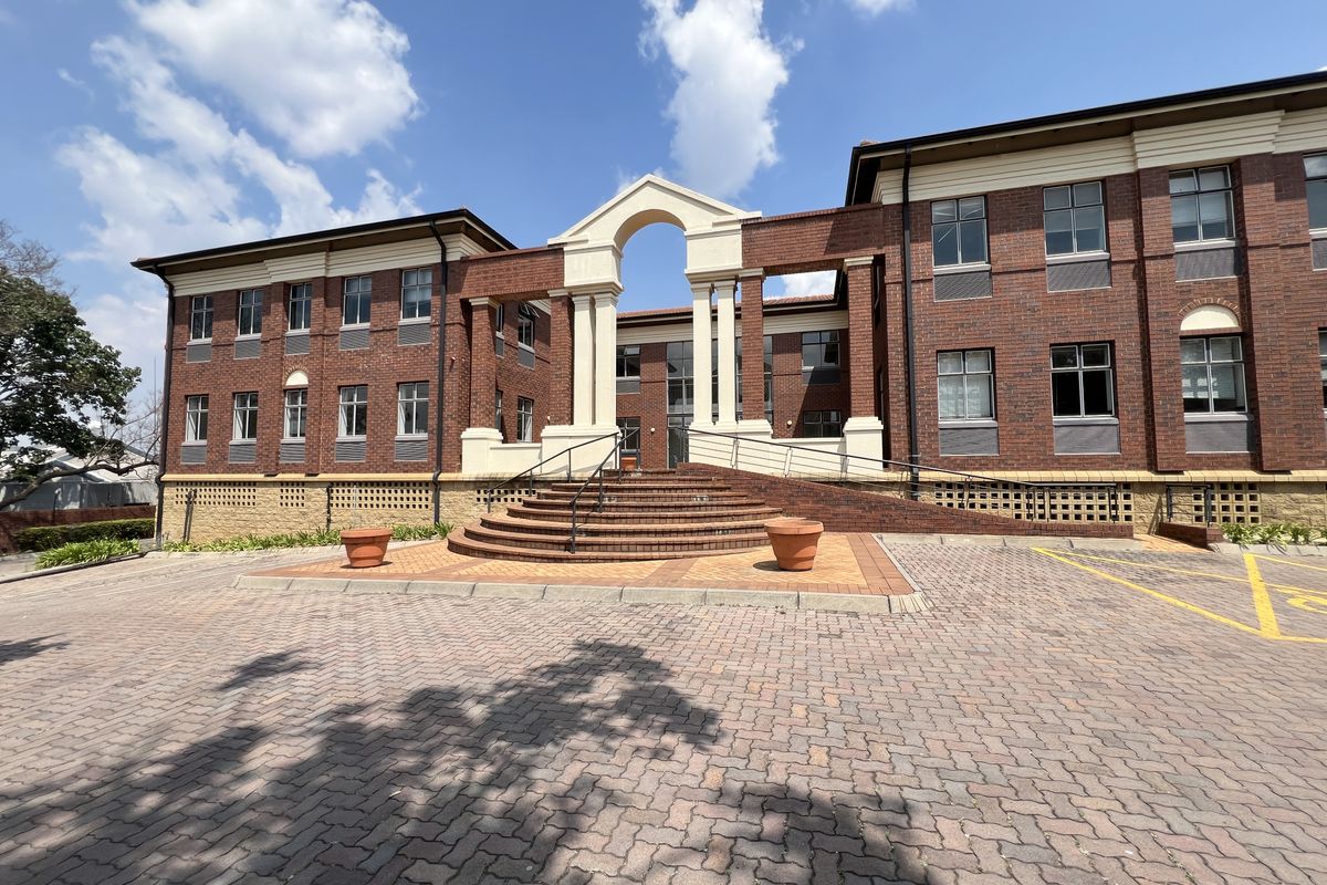 A professional office building featuring a classic red brick facade, a prominent arched entrance with stone steps, and a paved parking area.