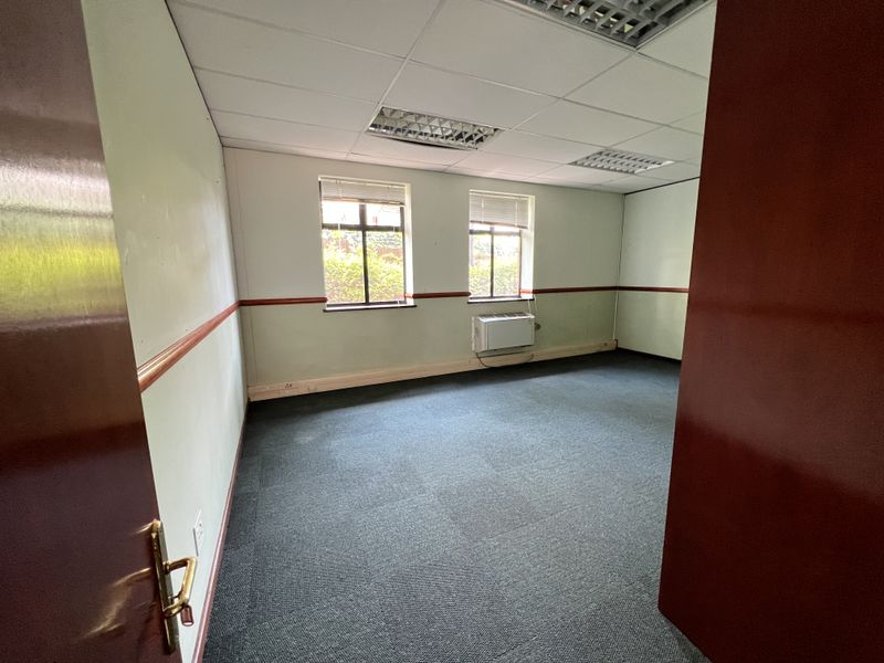 A vacant office space featuring carpeted flooring, suspended ceiling with recessed lighting, and a wall-mounted HVAC unit.
