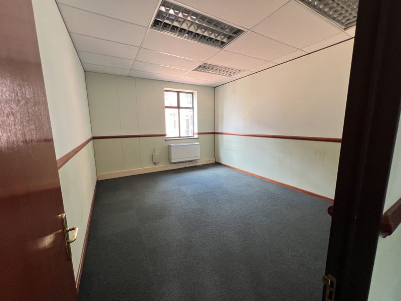 An empty office space featuring a suspended ceiling, recessed lighting, wall-mounted air conditioning, and carpeted flooring.