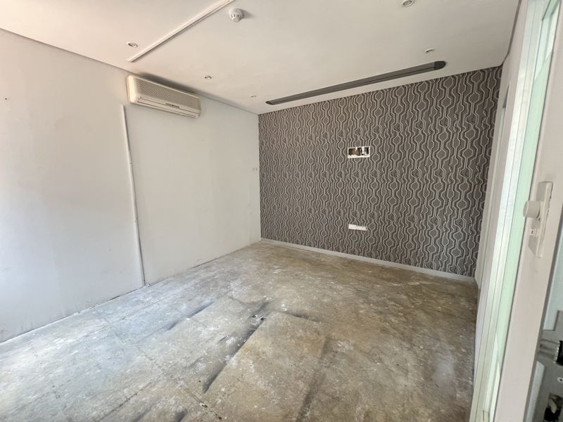 An empty office space featuring patterned wallpaper, recessed lighting, and an air conditioning unit, currently requiring new flooring installation.