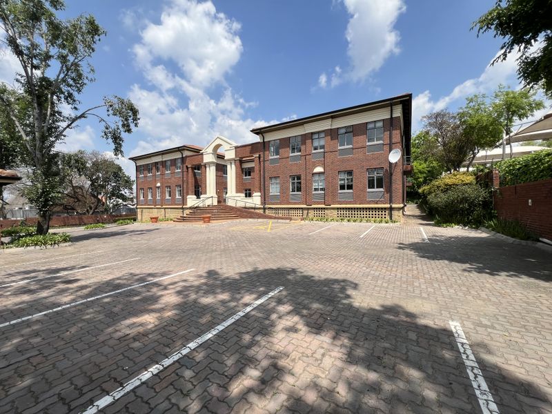 A professional exterior view of a multi-story brick office building featuring a paved parking lot and a prominent arched entrance.