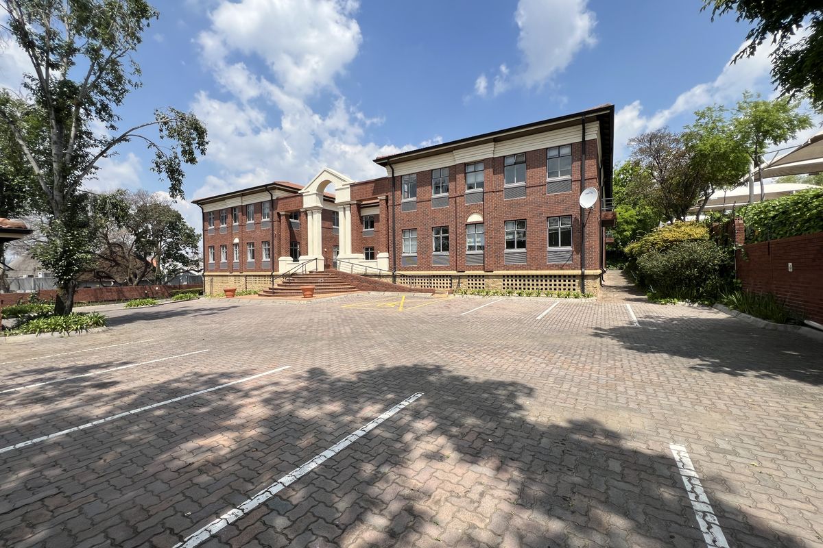 A professional exterior view of a multi-story brick office building featuring a paved parking lot and a prominent arched entrance.