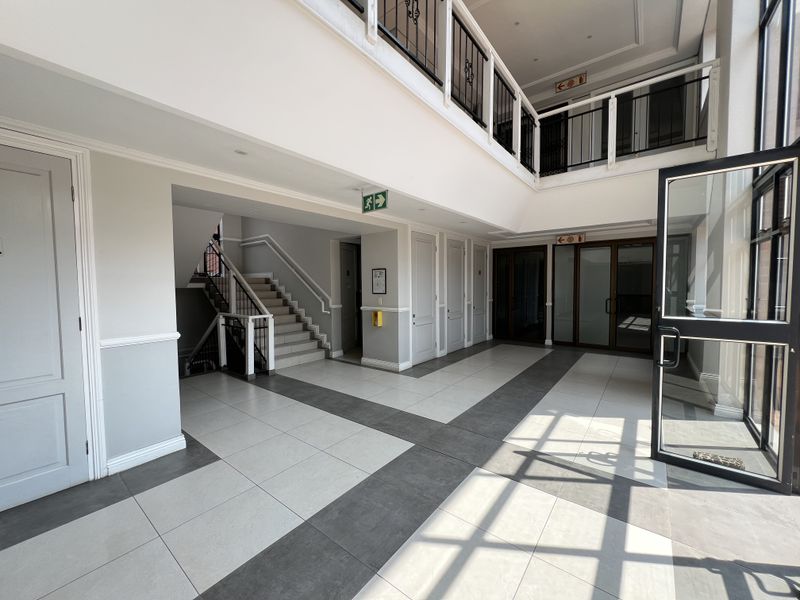 Spacious and bright office building entrance lobby featuring modern tiled flooring, a central staircase with wrought iron balustrades, and glass-paneled access doors.