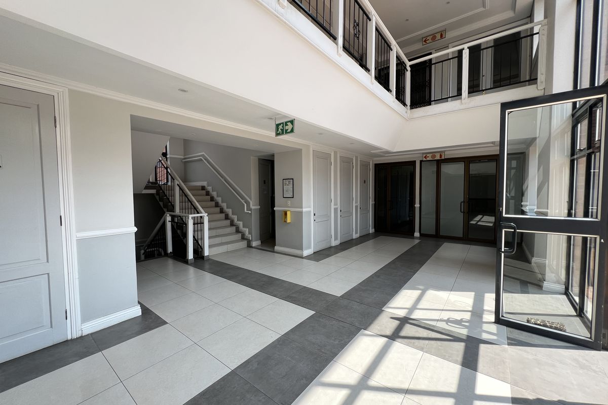 Spacious and bright office building entrance lobby featuring modern tiled flooring, a central staircase with wrought iron balustrades, and glass-paneled access doors.