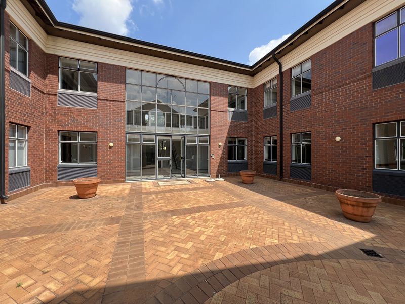 A well-maintained brick-faced office courtyard featuring a central glass entrance, paved flooring, and integrated exterior lighting.