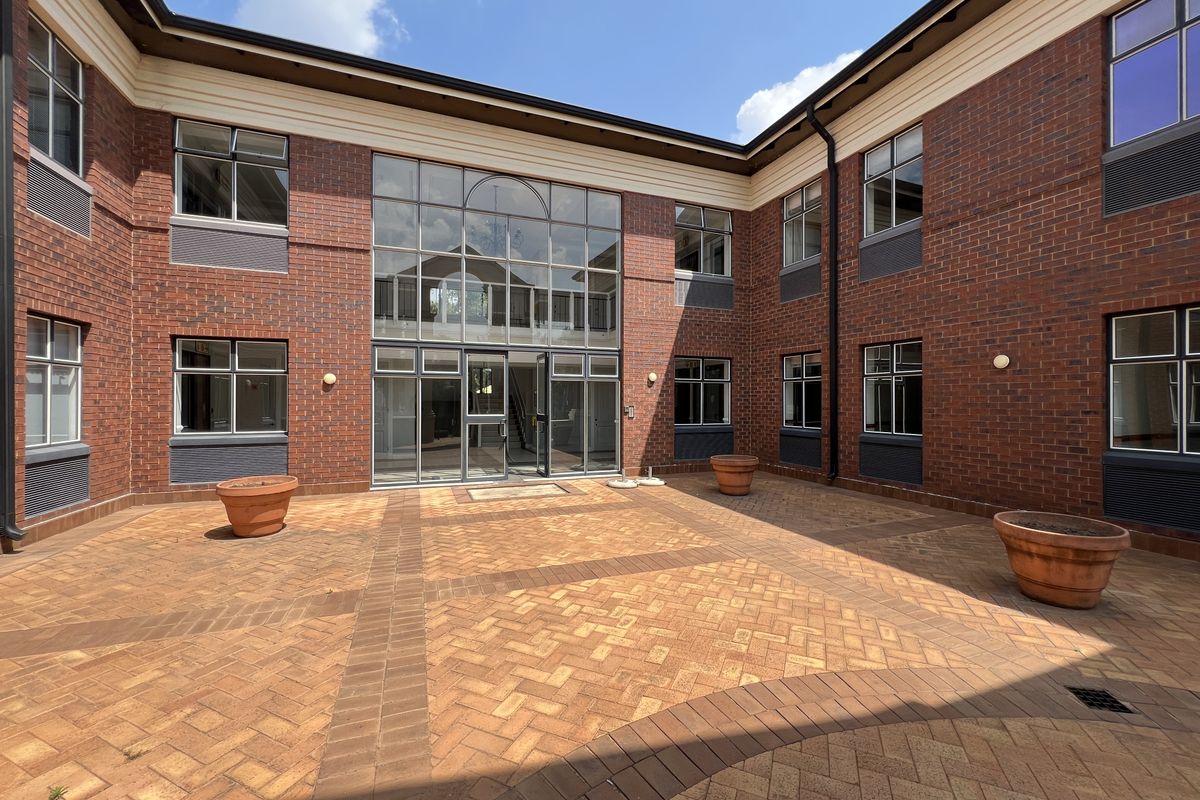 A well-maintained brick-faced office courtyard featuring a central glass entrance, paved flooring, and integrated exterior lighting.